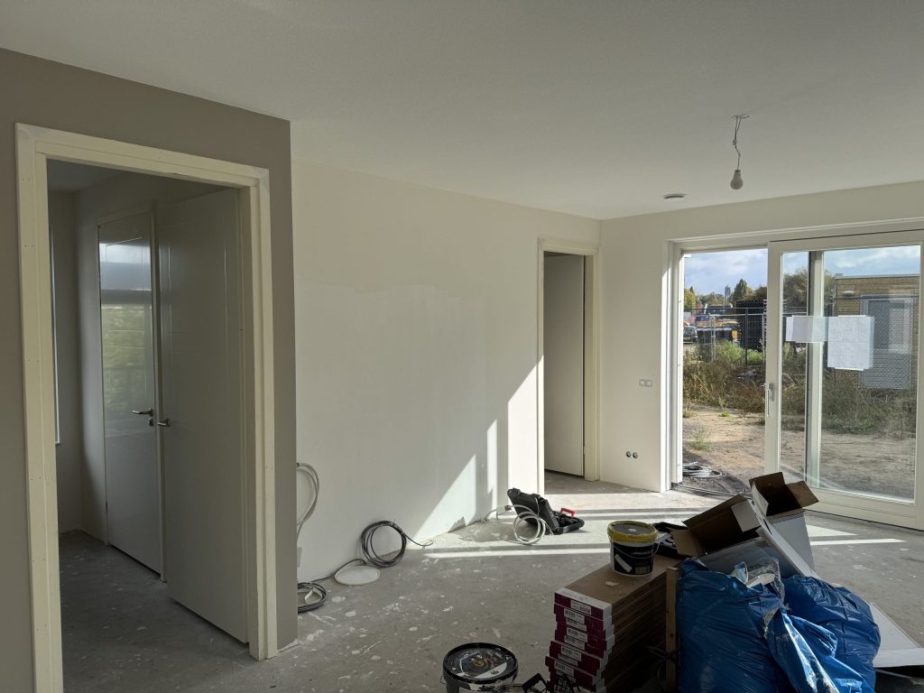 Opgeleverde nieuwbouwwoning met kale wanden, schuifpui naar de tuin en materiaal op de vloer