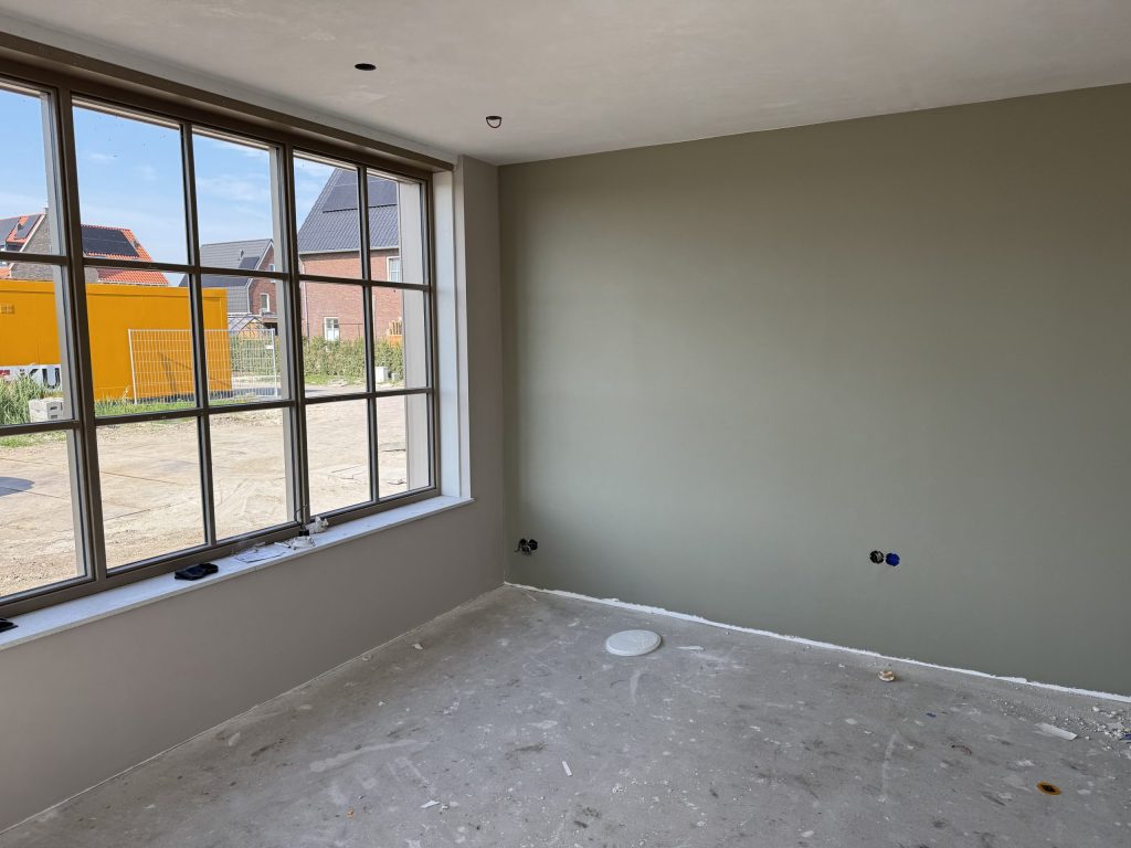 Kamer met groot raam met roedes en een egaal groen gesausde wand op renovlies