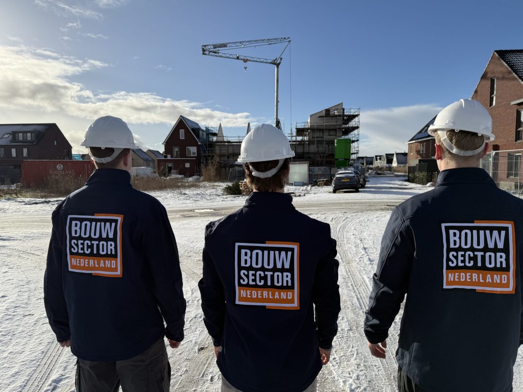 Drie medewerkers van Bouwsector Nederland met witte helm op weg naar een nieuwbouwproject in de sneeuw